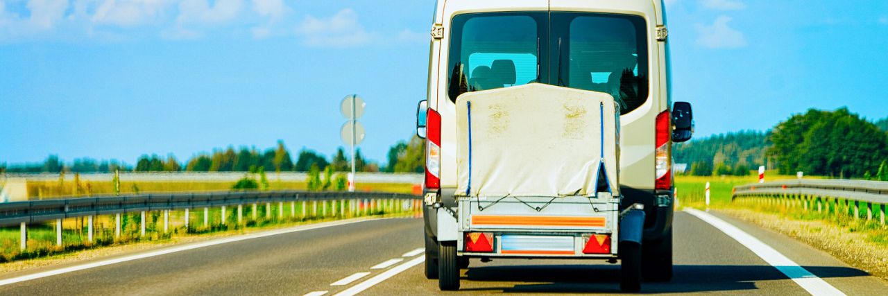 A&J Anhängerverleih – Wenn der Einkauf etwas größer geworden ist, helfen wir Ihnen gern! Heckansicht eines Transporters mit kleinem Anhänger auf einer Landstraße umgeben von Feldern