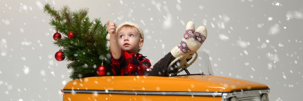 A&J Weihnachtsbaum-Verkauf – Jedes Jahr kleine und große Nordmanntannen zu günstigen Preisen » Ein kleiner Junge sitzt mit einem geschmückten, kleinen Tannenbaum in einem Tretauto